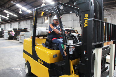 smiling worker driving forklift of steel channel on factory floor